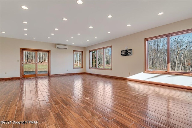 unfurnished living room featuring an AC wall unit, plenty of natural light, and wood finished floors