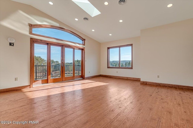 empty room with vaulted ceiling with skylight, baseboards, visible vents, and light wood finished floors