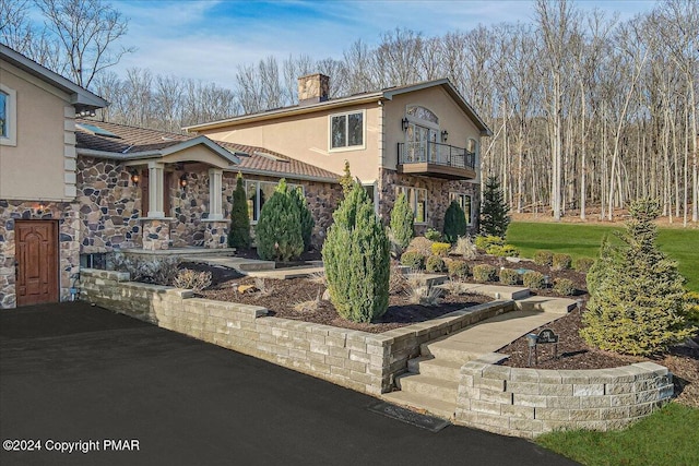 view of front of home with a chimney, stone siding, a balcony, and stucco siding