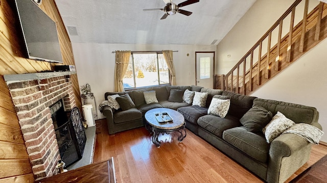 living room featuring ceiling fan, a textured ceiling, a brick fireplace, wood-type flooring, and lofted ceiling