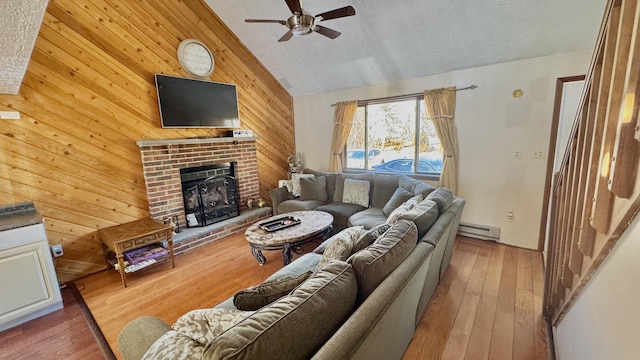 living room featuring a brick fireplace, ceiling fan, wooden walls, a baseboard radiator, and vaulted ceiling