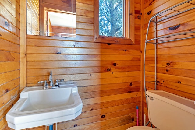 half bath featuring toilet, wood walls, and a sink
