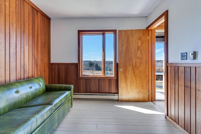 unfurnished room with wood walls, a baseboard radiator, wood-type flooring, and a wainscoted wall