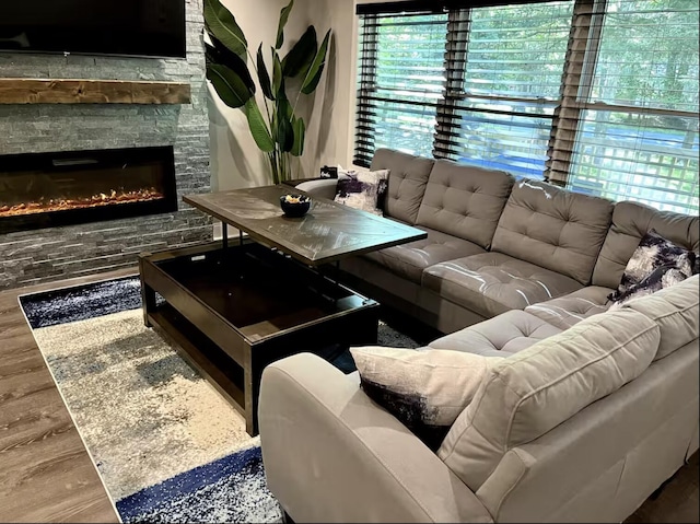 living area with a stone fireplace, a healthy amount of sunlight, and wood finished floors