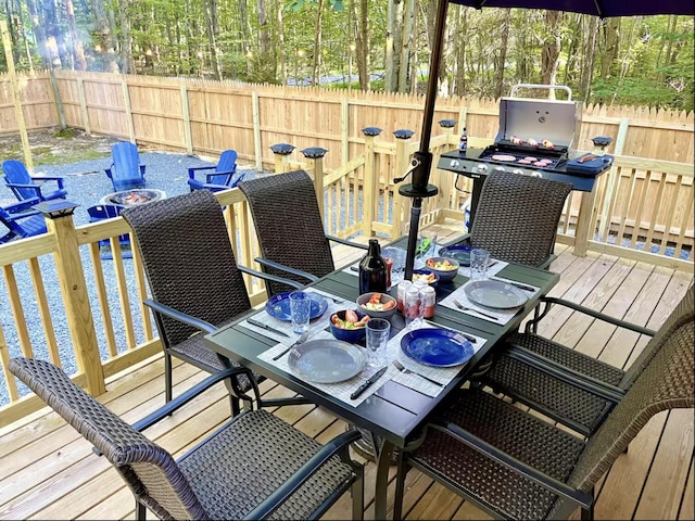 wooden deck with a fenced backyard, an outdoor fire pit, outdoor dining space, and a water view