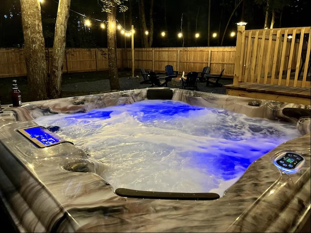 pool at night with a fenced backyard and a hot tub