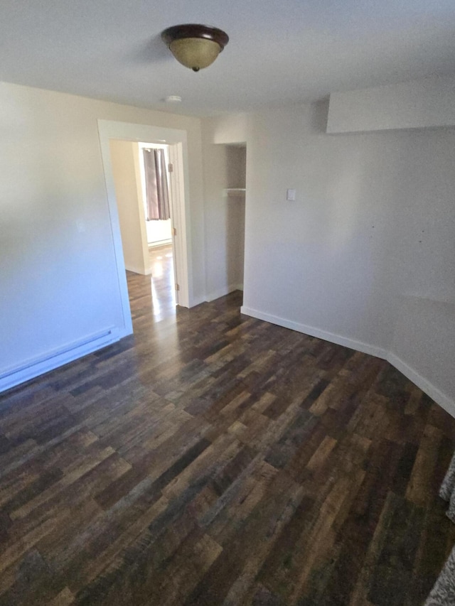 empty room with dark wood-type flooring, baseboards, and baseboard heating