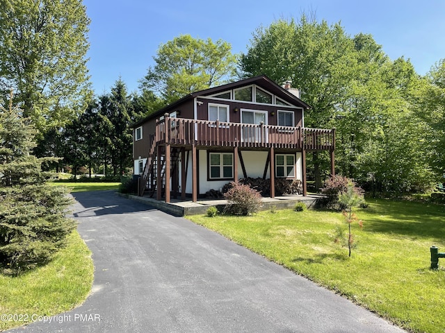 view of front of property with a front yard, stairway, a chimney, stucco siding, and a deck