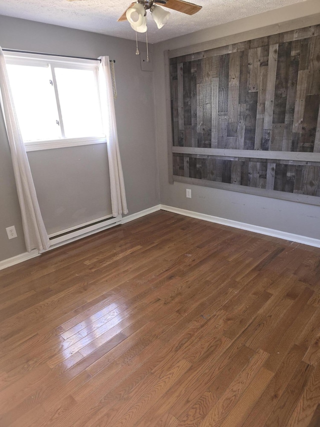 empty room featuring wood finished floors, baseboard heating, ceiling fan, a textured ceiling, and baseboards