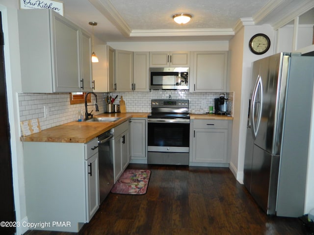 kitchen featuring wood counters, sink, crown molding, hanging light fixtures, and stainless steel appliances