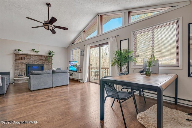 dining space with a textured ceiling, a ceiling fan, vaulted ceiling, light wood-type flooring, and a brick fireplace
