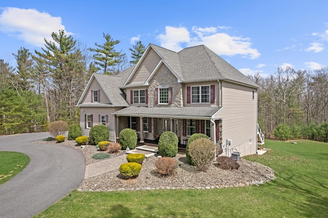 view of front of property featuring a front yard, roof with shingles, stone siding, and covered porch