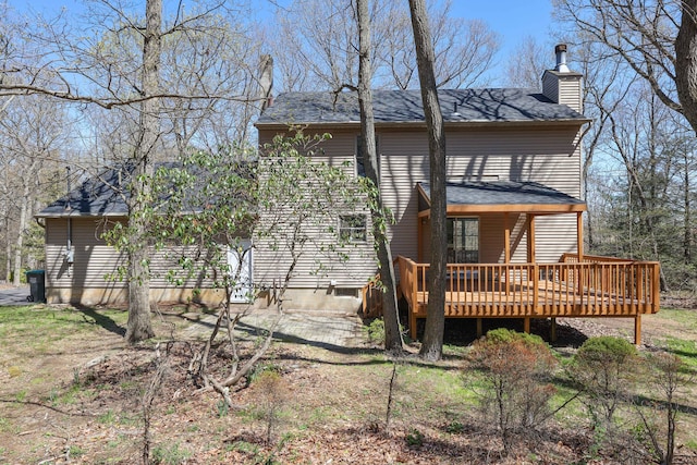 back of house featuring roof with shingles, a wooden deck, and a chimney