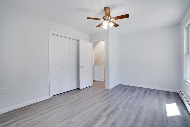unfurnished bedroom featuring ceiling fan, baseboard heating, wood finished floors, baseboards, and a closet
