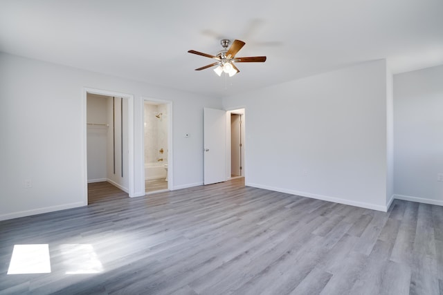 unfurnished bedroom with baseboards, a walk in closet, wood finished floors, and a closet