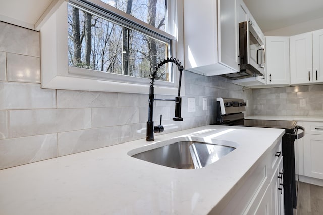 kitchen with a sink, backsplash, white cabinets, and stainless steel appliances