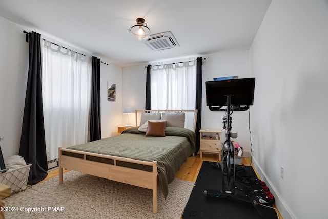 bedroom with light wood finished floors, visible vents, a baseboard heating unit, and baseboards