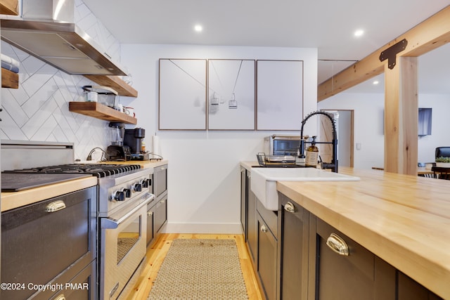 kitchen with light wood-style flooring, wood counters, high end stainless steel range oven, decorative backsplash, and wall chimney exhaust hood