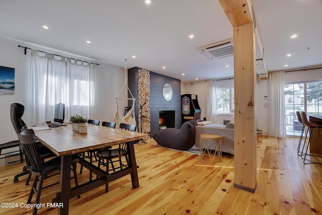 dining space featuring a large fireplace, light wood finished floors, a wall unit AC, and recessed lighting