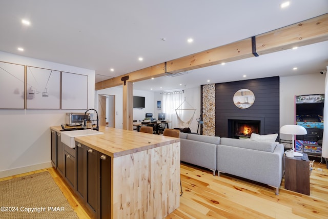 kitchen with beam ceiling, a fireplace, butcher block counters, light wood-style floors, and a sink