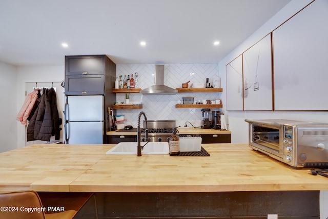 kitchen featuring a toaster, open shelves, wooden counters, freestanding refrigerator, and wall chimney exhaust hood