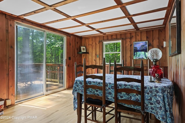 dining area featuring coffered ceiling, light wood-style flooring, and wooden walls