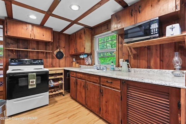 kitchen featuring stainless steel microwave, electric range oven, a sink, wood walls, and light wood-type flooring