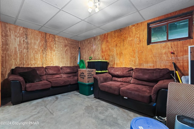 living room featuring concrete floors, a drop ceiling, and wood walls