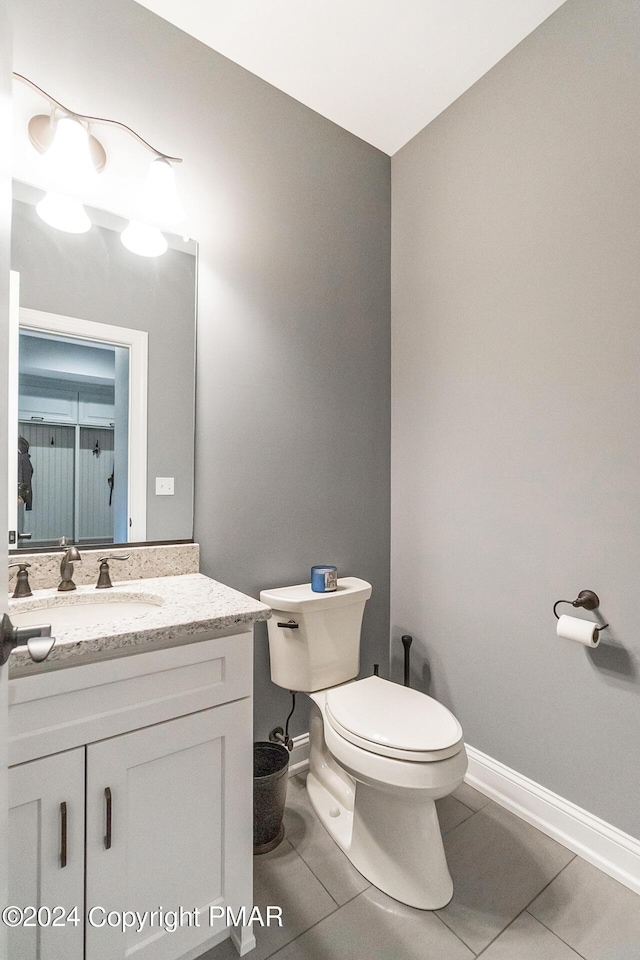 half bathroom featuring toilet, vanity, baseboards, and tile patterned floors