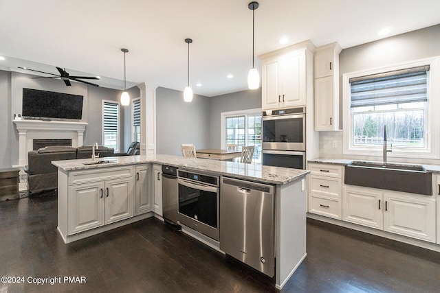 kitchen with a fireplace, appliances with stainless steel finishes, light stone counters, and a sink