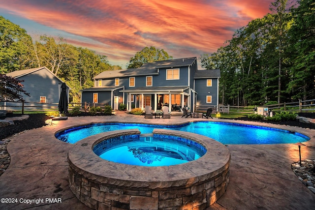 pool at dusk featuring a patio area, fence, and a pool with connected hot tub