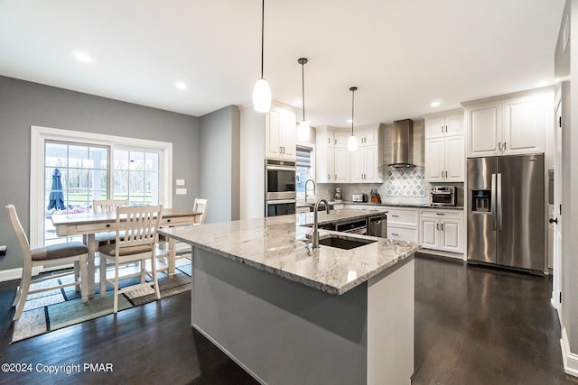 kitchen with decorative backsplash, appliances with stainless steel finishes, a sink, wall chimney range hood, and light stone countertops