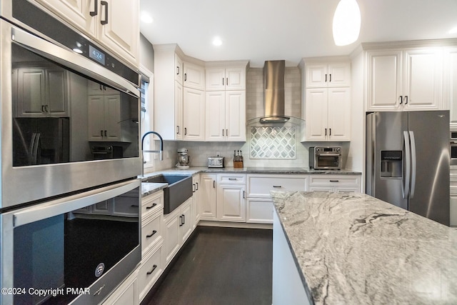 kitchen with white cabinets, wall chimney exhaust hood, light stone counters, stainless steel appliances, and a sink