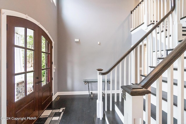 foyer entrance featuring arched walkways, french doors, a towering ceiling, and baseboards