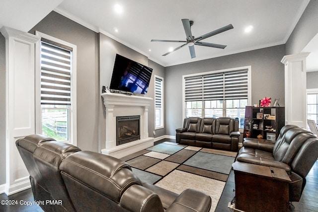 living room featuring baseboards, a fireplace with raised hearth, a ceiling fan, ornamental molding, and ornate columns