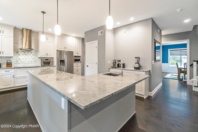 kitchen featuring visible vents, decorative backsplash, wall chimney exhaust hood, stainless steel appliances, and a sink