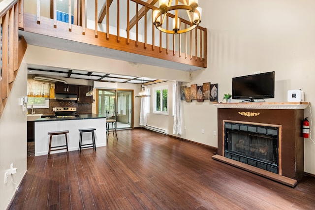 205 Victory Ln, Long Pond, PA 18334 - unfurnished living room with a chandelier, a baseboard heating unit, a fireplace with raised hearth, dark wood-style floors, and a towering ceiling