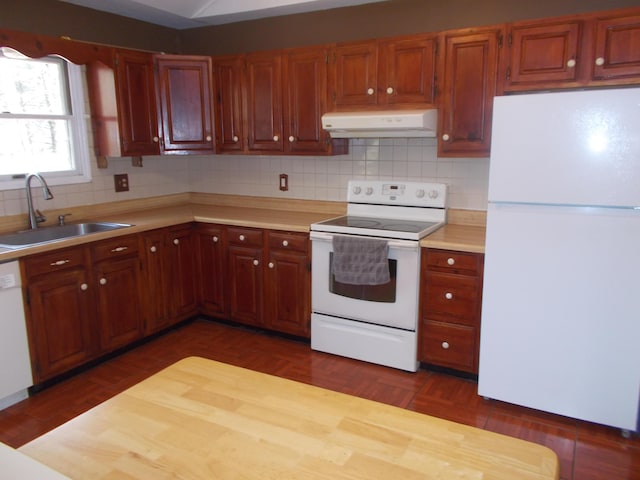 kitchen with a sink, light countertops, under cabinet range hood, white appliances, and backsplash