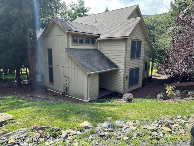 view of side of property with board and batten siding, roof with shingles, and a yard