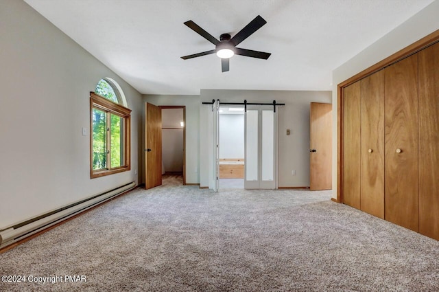 unfurnished bedroom featuring baseboard heating, ensuite bathroom, a barn door, light carpet, and ceiling fan