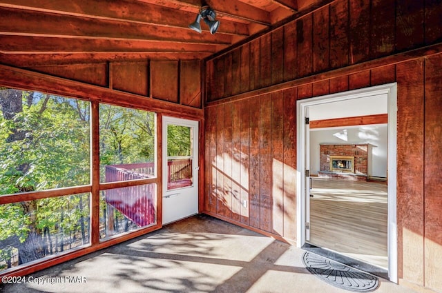 unfurnished sunroom with vaulted ceiling with beams, a brick fireplace, and plenty of natural light