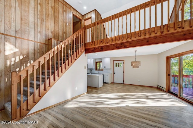 unfurnished living room featuring a baseboard heating unit, a towering ceiling, baseboards, light wood-style floors, and stairway