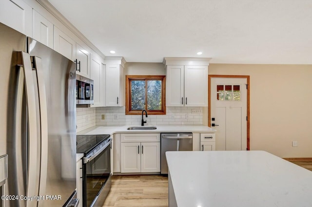 kitchen featuring white cabinets, a sink, stainless steel appliances, light countertops, and backsplash