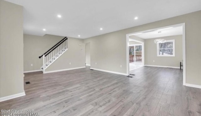 unfurnished living room with baseboards, wood finished floors, stairs, a chandelier, and recessed lighting