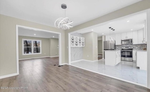 unfurnished living room with recessed lighting, a notable chandelier, light wood-style flooring, and baseboards