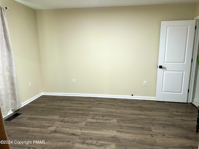 empty room featuring dark wood-style flooring, visible vents, and baseboards