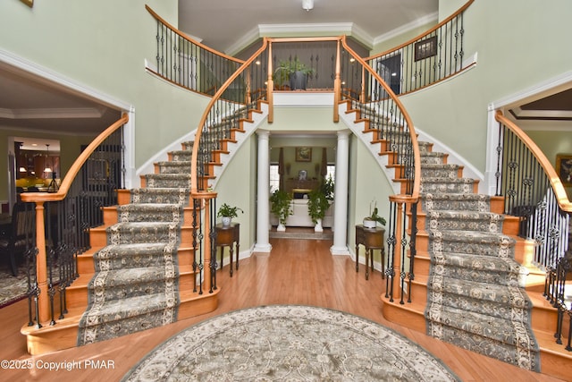 stairway featuring decorative columns, wood finished floors, and ornamental molding