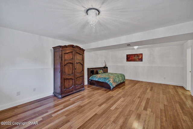 bedroom featuring an inviting chandelier, baseboards, and light wood-type flooring