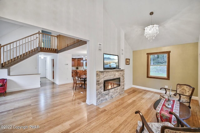 living area featuring baseboards, a fireplace, wood finished floors, a notable chandelier, and a high ceiling