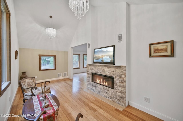 living area featuring wood finished floors, a fireplace, baseboards, visible vents, and a notable chandelier